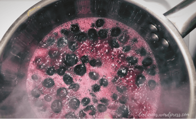 Boiling blueberries on the stove with red blueberry stained water foaming around the blueberries