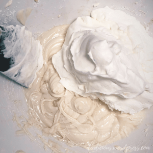 A deep bowl filled with a creamy filling and whipped cream dolloped on top with a spatula going into the bowl