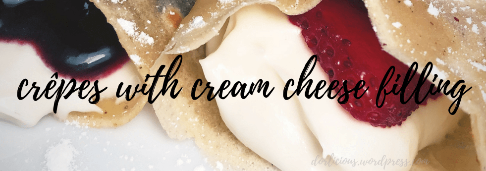 close up photo of two crêpes filled with cream cheese filling and stuffed with blueberry compote and slice strawberries then lightly dusted with confectioners sugar