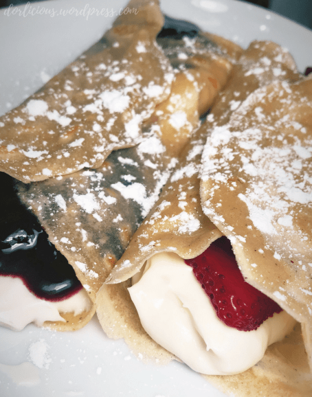 Crêpes filled with cream cheese filling, strawberries and blueberry compote that are plated and lightly dusted with confectioners sugar
