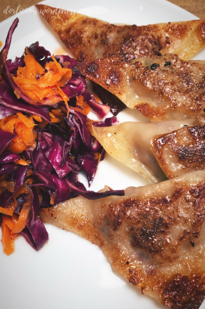 Browned potstickers on a white plate with pickled red cabbage and carrot slaw