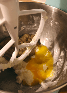 image of beaten eggs, creamed sugar and butter and mashed bananas inside a metal bowl of a stand mixer with a white beater in frame