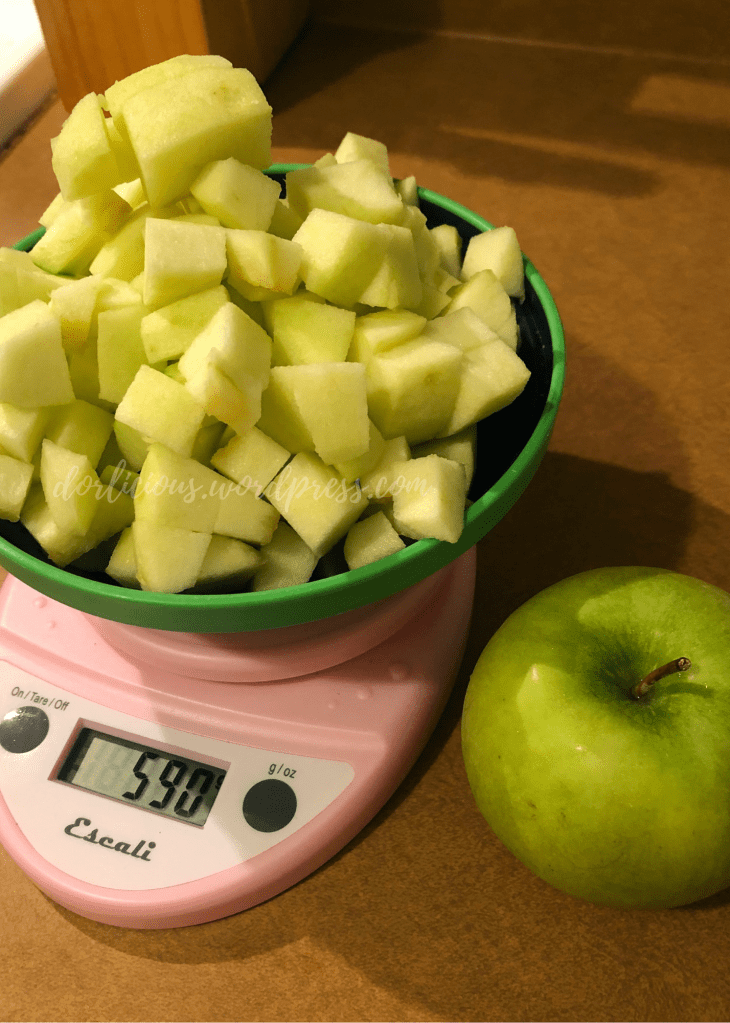 granny smith apples chopped up in a bowl on a scale with a whole apple next to it